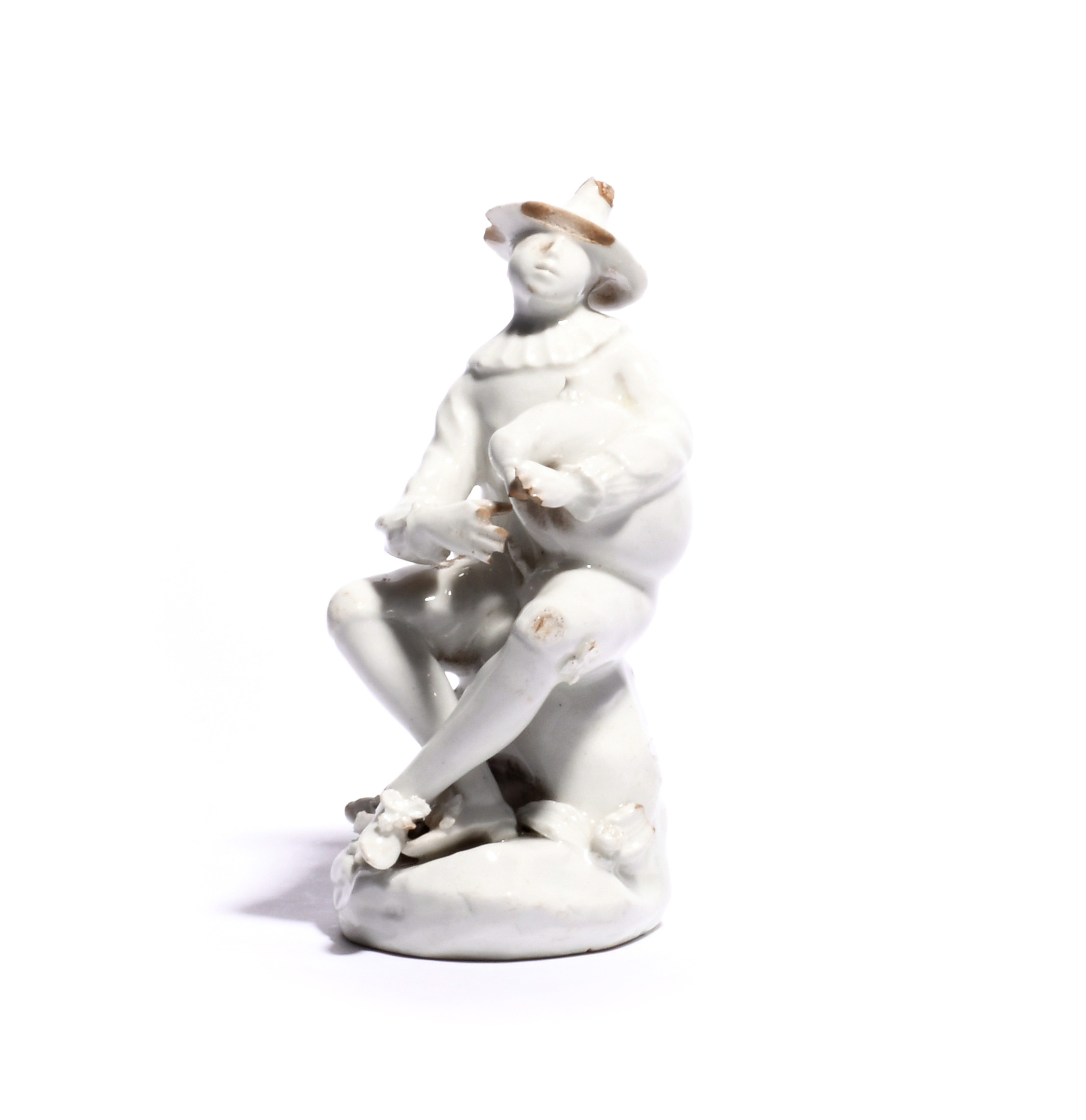 A Bow white-glazed figure of Harlequin c.1753-55, after the Meissen model by J J Kändler, seated