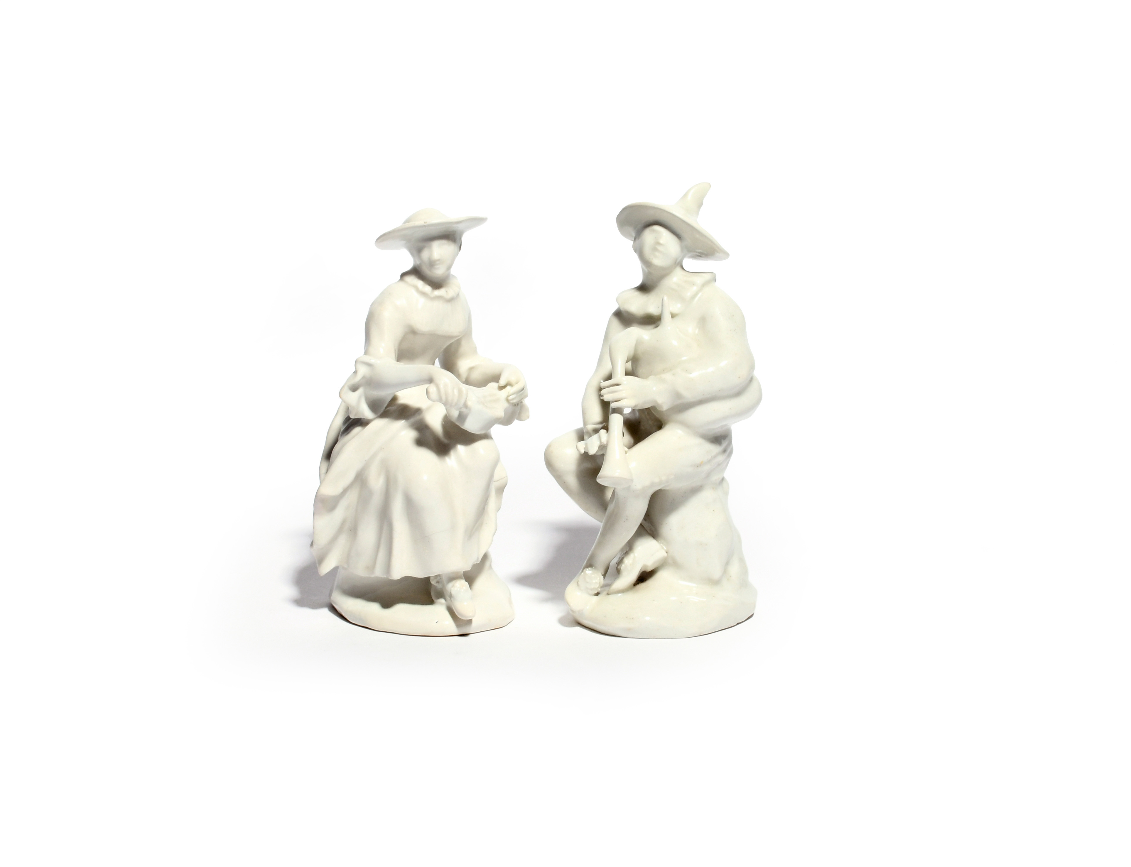 A pair of white-glazed Bow figures of Harlequin and Columbine c.1755-60, seated on rocky stumps,