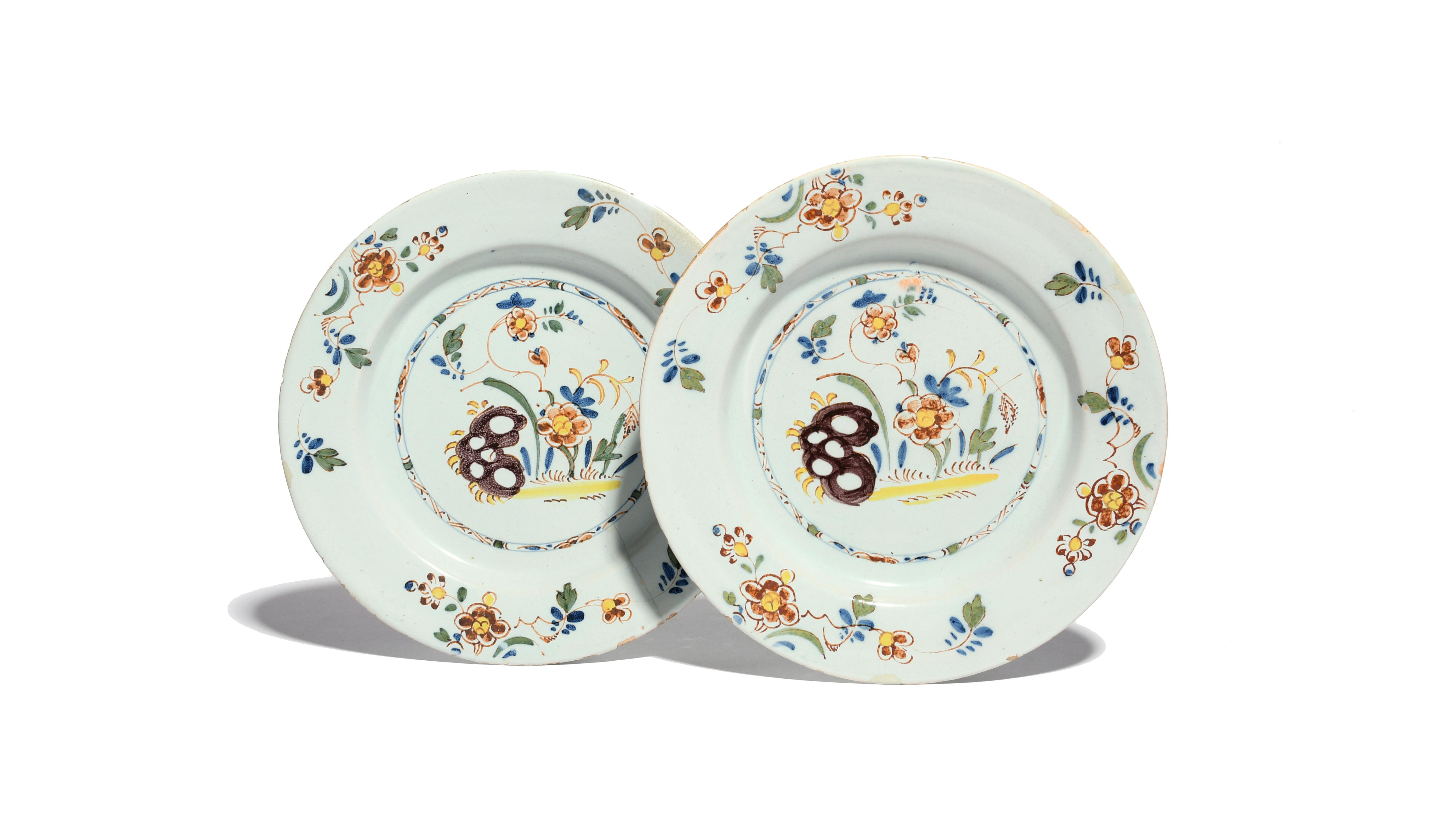 A pair of delftware plates c.1760, painted in polychrome enamels with flowering plants and holey