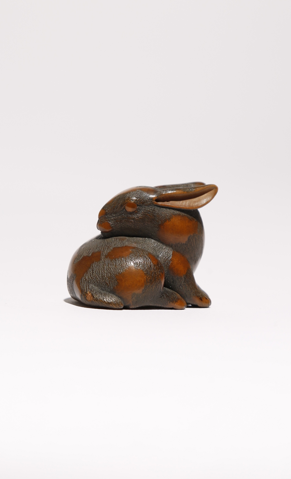 A JAPANESE WOOD NETSUKE OF A HARE WITH AMBER EYES EDO PERIOD, 19TH CENTURY Recumbant and with its