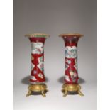 A NEAR PAIR OF CHINESE FAMILLE ROSE RUBY-GROUND ORMOLU-MOUNTED BEAKER VASES THE PORCELAIN 18TH