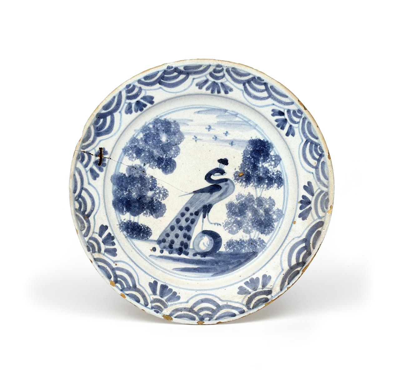 A Delft charger c.1680-90, painted in blue with a strutting peacock flanked by tall sponged trees,
