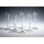 Six wine flutes c.1760, the slender drawn trumpet bowls with slightly everted rims, rising from