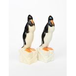 A pair of Geo Conde pottery penguins, each cast standing on an ice block, glazed in colours, cast