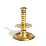 A SMALL CHARLES II BRASS TRUMPET CANDLESTICK C.1650-80 with a ribbed stem and a central drip-pan,