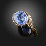 A sapphire and diamond ring, the oval-shaped sapphire is set within scrolling shoulders with rose-