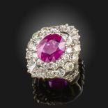 A ruby and diamond cluster ring, the oval-shaped ruby is set within a surround of round brilliant-