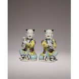 A PAIR OF CHINESE FAMILLE ROSE MODELS OF SEATED BOYS 18TH CENTURY Wearing yellow jackets decorated