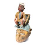 A Yoruba gelede mask Nigeria surmounted with a male figure, wearing a cap and sitting on a folding