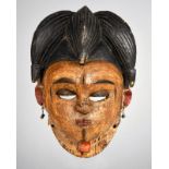 An Ibibio mask Nigeria with bead earrings and pigment, 25.5cm high.