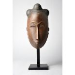 A Baule mask Ivory Coast finely carved with a quadripartite domed and ebonised coiffure and with