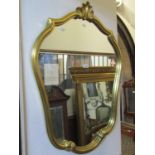 A contemporary shield shaped wall mirror, the moulded and scrolled gilt frame with shell surmount,