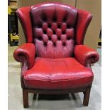 A contemporary Georgian style red leather upholstered wing armchair with button back and loose squab