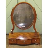 A Georgian mahogany toilet mirror, the oval mirror plate raised on shaped supports, the serpentine