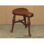A walnut saddle shaped stool raised on three turned legs united by stretchers, stamped underneath
