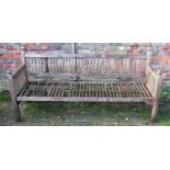 A weathered teak garden bench with slatted back and arms beneath faceted finials (AF), 6ft long