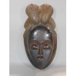 Tribal interest - a carved wooden mask/wall hanging in the form of a head with feathered head dress,