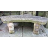 A weathered cast composition stone three sectional garden bench with curved slab seat, raised on