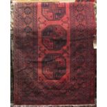 An Afghan wool rug, principally in a red and black colourway, the central lozenge shaped medallion