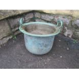 A weathered copper with two fixed loop handles flared folded rim, riveted band and rounded bottom,