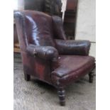 A late Victorian/Edwardian wing armchair raised on turned forelegs with tired leather upholstery (