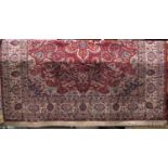 A Persian style carpet with red ground, scrolled floral detail and set within repeating running