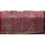 A Persian style wool carpet with red ground, abstract floral decoration, set within geometric