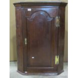 A Georgian oak hanging corner cupboard enclosed by a fielded arched panelled door with polished H