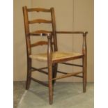 A stained beechwood open elbow chair with ladderback over a rush seat and simple turned supports and