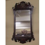 A Georgian mahogany wall mirror with shaped and fretted framework enclosing a circular carved and