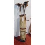 A vintage canvas and leather banded golf bag containing a number of vintage golf clubs