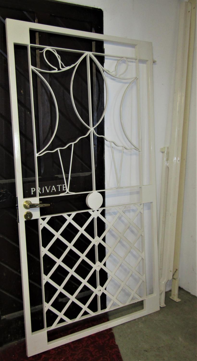 A cream painted security gate, with decorative lattice and further detail, handle lock and key (