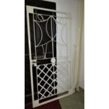A cream painted security gate, with decorative lattice and further detail, handle lock and key (