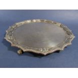 A silver salver in the Georgian style with shaped border, raised on three lions paw feet, 21cm