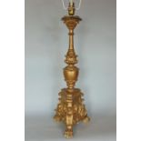 A gilt wood and gesso floorstanding lamp, with triform plateau, carved with flowerhead and paw