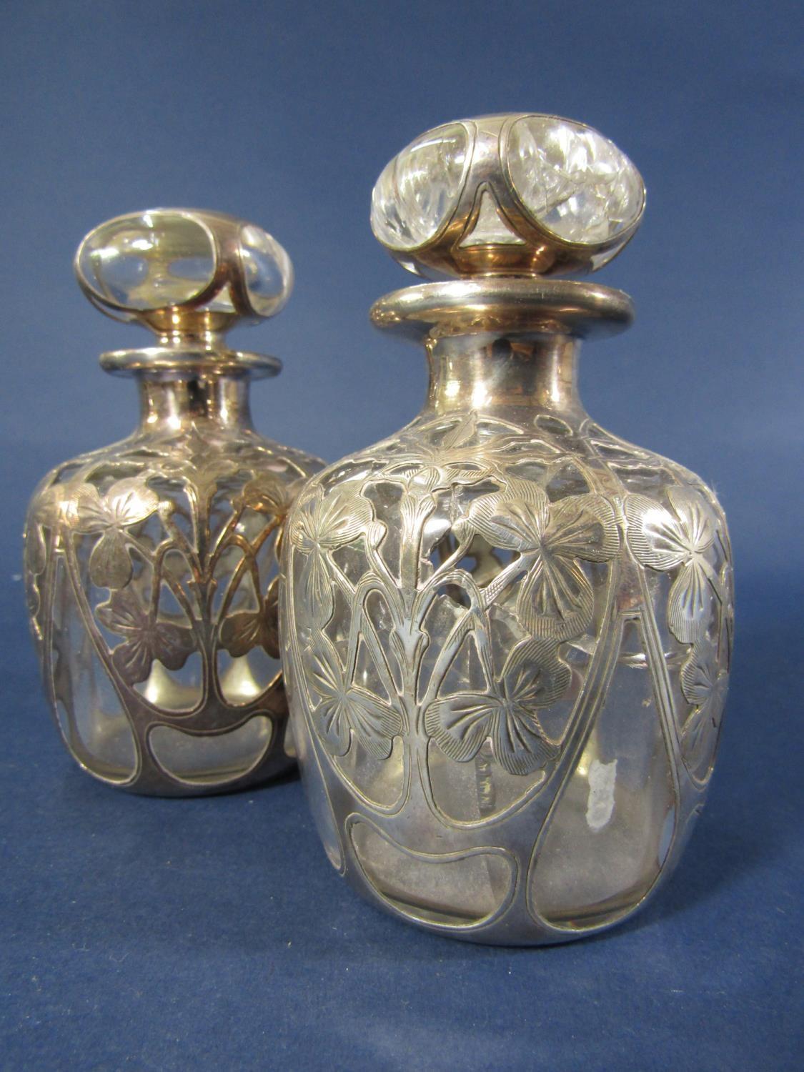 A pair of silver overlaid glass toilet water bottles with repeating foliate details, 12cm high