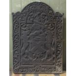 A cast iron fireback of stepped arched form, with raised relief armorial detail, Latin script and