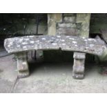 A weathered reclaimed three sectional garden bench with curved slab seat raised on a pair of