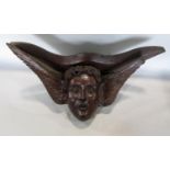 A carved oak wall hanging or bracket in the form of a winged cherubs face, 37cm long