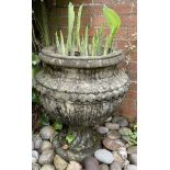 A reclaimed garden urn with squat drawn neck fluted bowl and repeating bead band raised on a wrythen