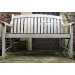 A weathered teak two seat garden bench with curved drop in slatted seat and back beneath an arched