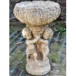 A reclaimed garden planter in the form of three cherubs supporting a circular acanthus leaf bowl,