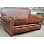 An early 20th century two seat sofa with rolled arms, tan faux leather upholstered finish with loose