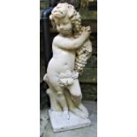 A reclaimed garden figure in the form of a standing cherub holding a bunch of grapes and standing