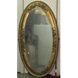 An oval gilt framed wall mirror with bevelled edge plate and applied tied ribbon and trailing rose