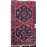 Persian full pile rug decorated with two geometric blue and green medallions upon a washed red