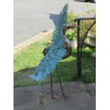 A contemporary painted tin garden ornament in the form of a standing stork, with wings outstretched,