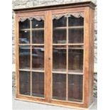 A late Victorian stripped oak side cabinet enclosed by a pair of segmented glazed panelled doors