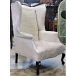 An Edwardian wing armchair with shaped outline simply upholstered in white calico type material,