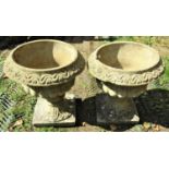 A pair of reclaimed garden urns, with flared rims, lobed bodies and square cut platform bases,
